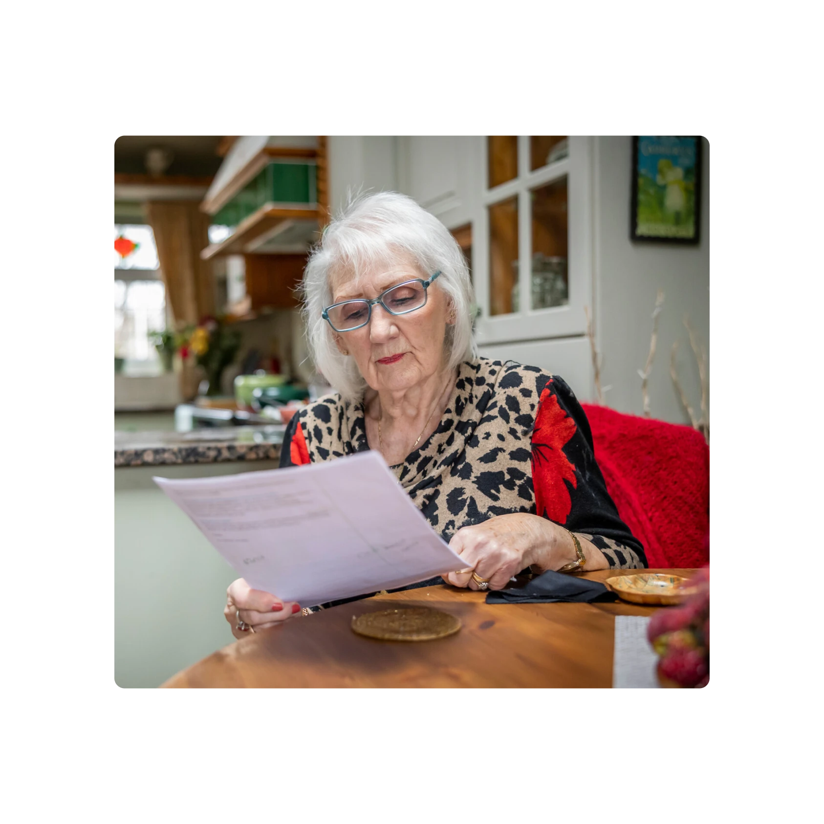 Photograph of an older woman reviewing some paperwork at a kitchen table.